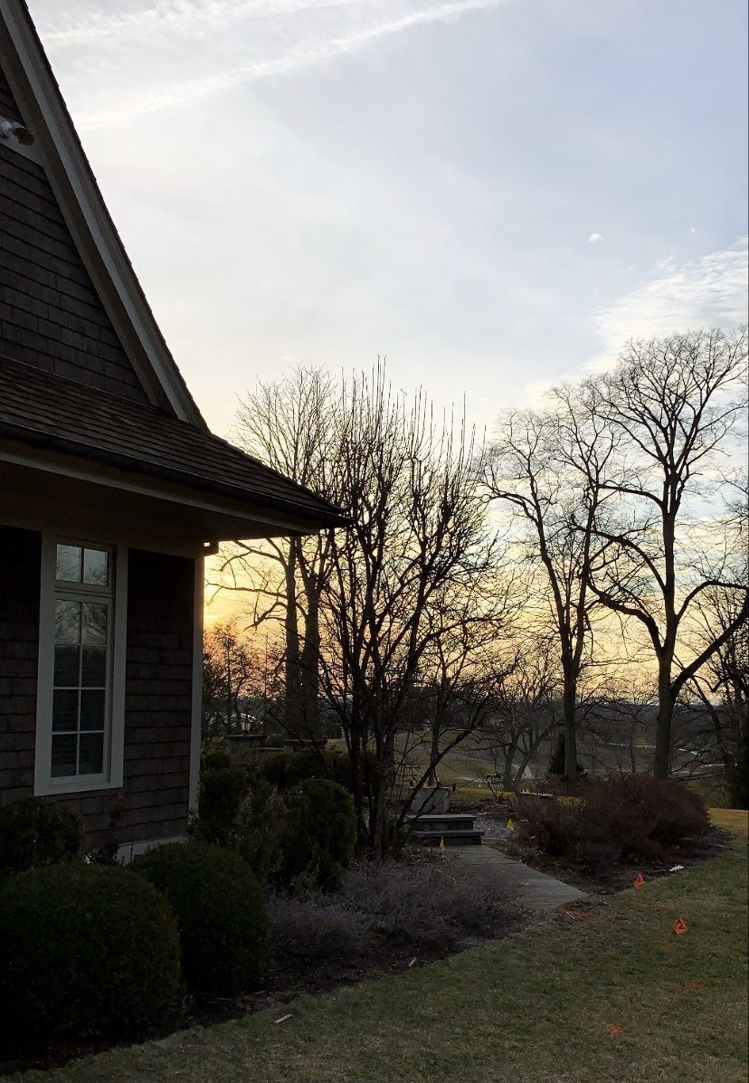A house with a sunset in the background and trees in the foreground