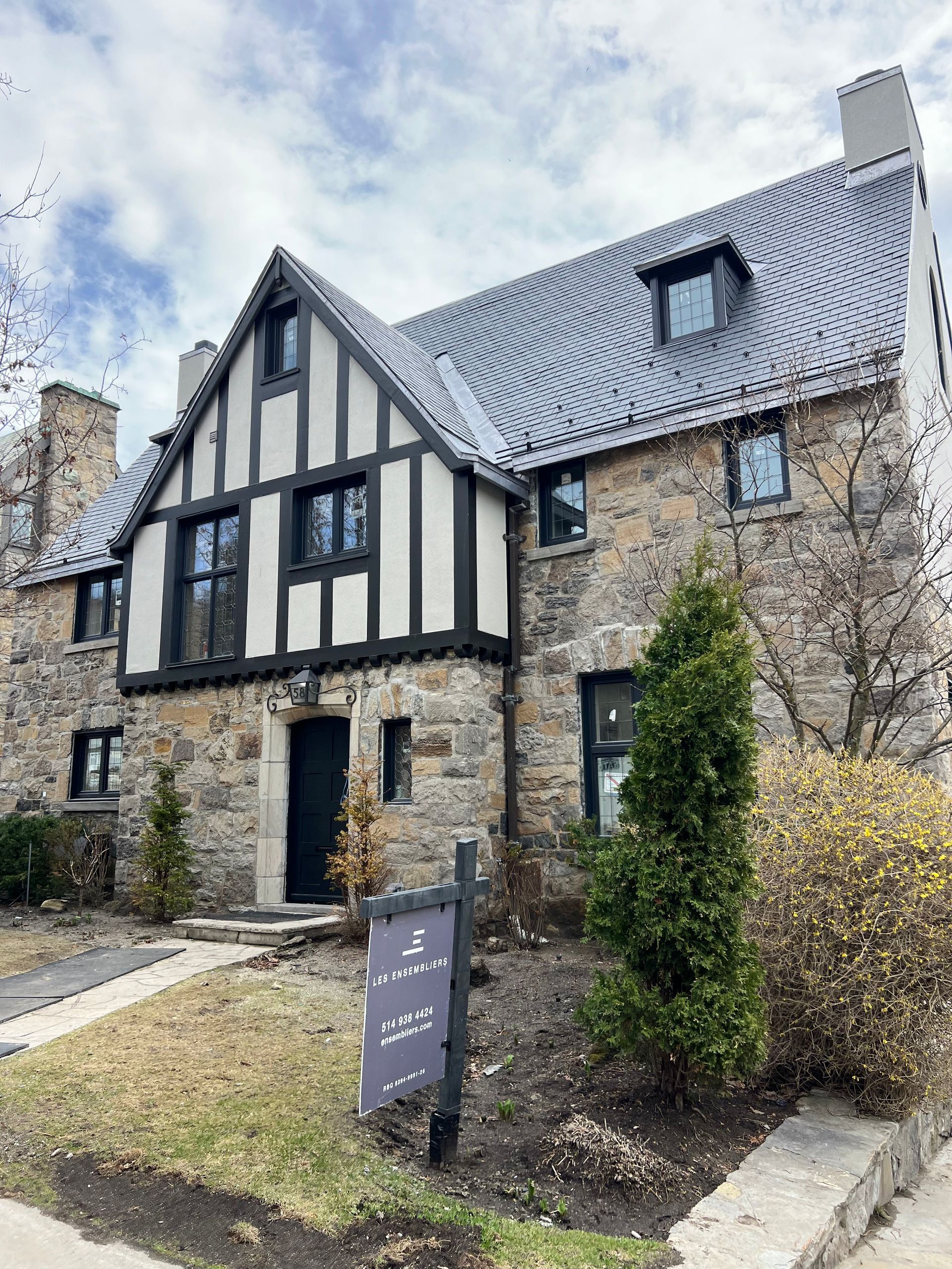 A large stone house with a for sale sign in front of it.