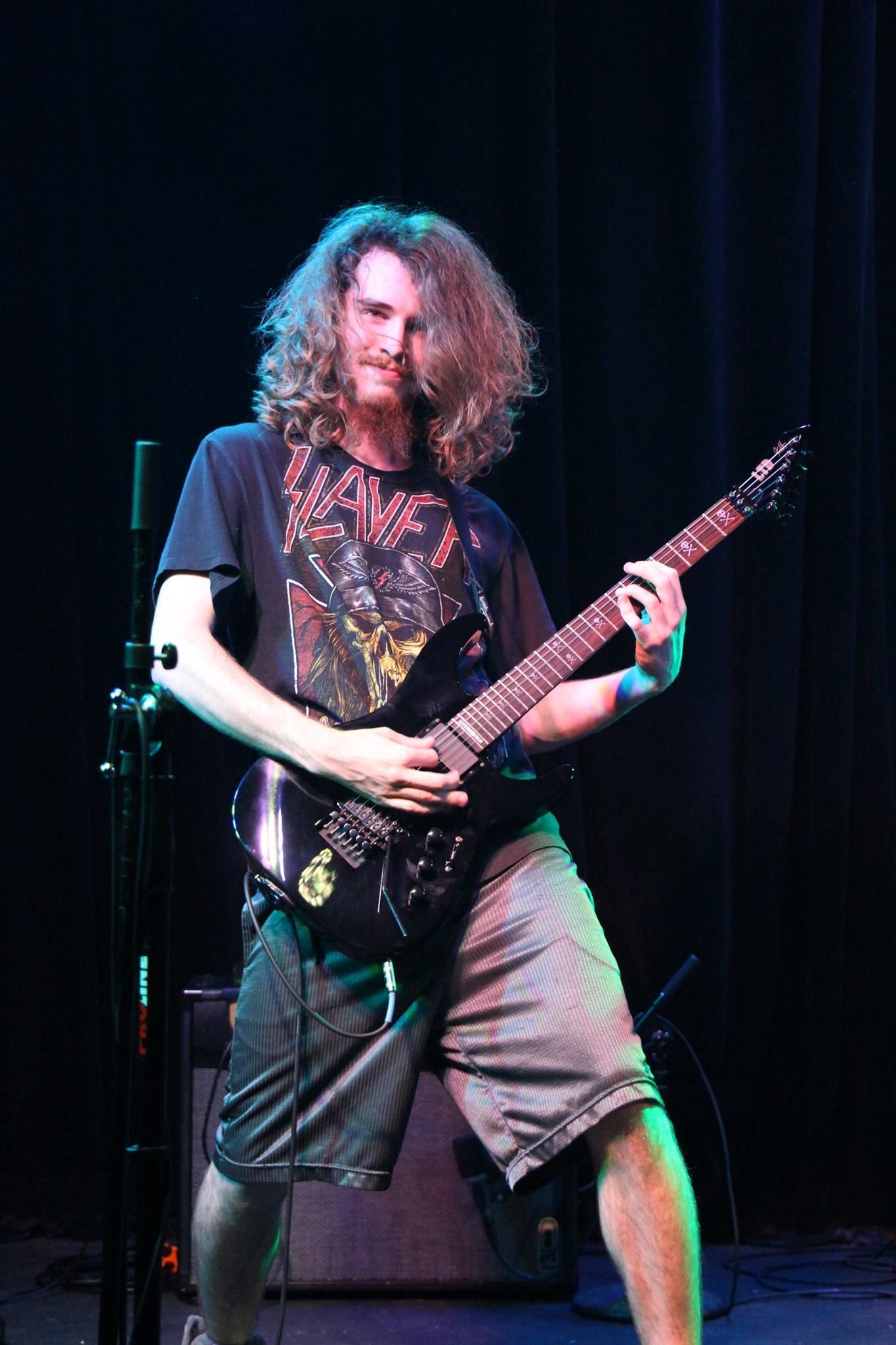A man with long hair is playing a guitar on a stage.