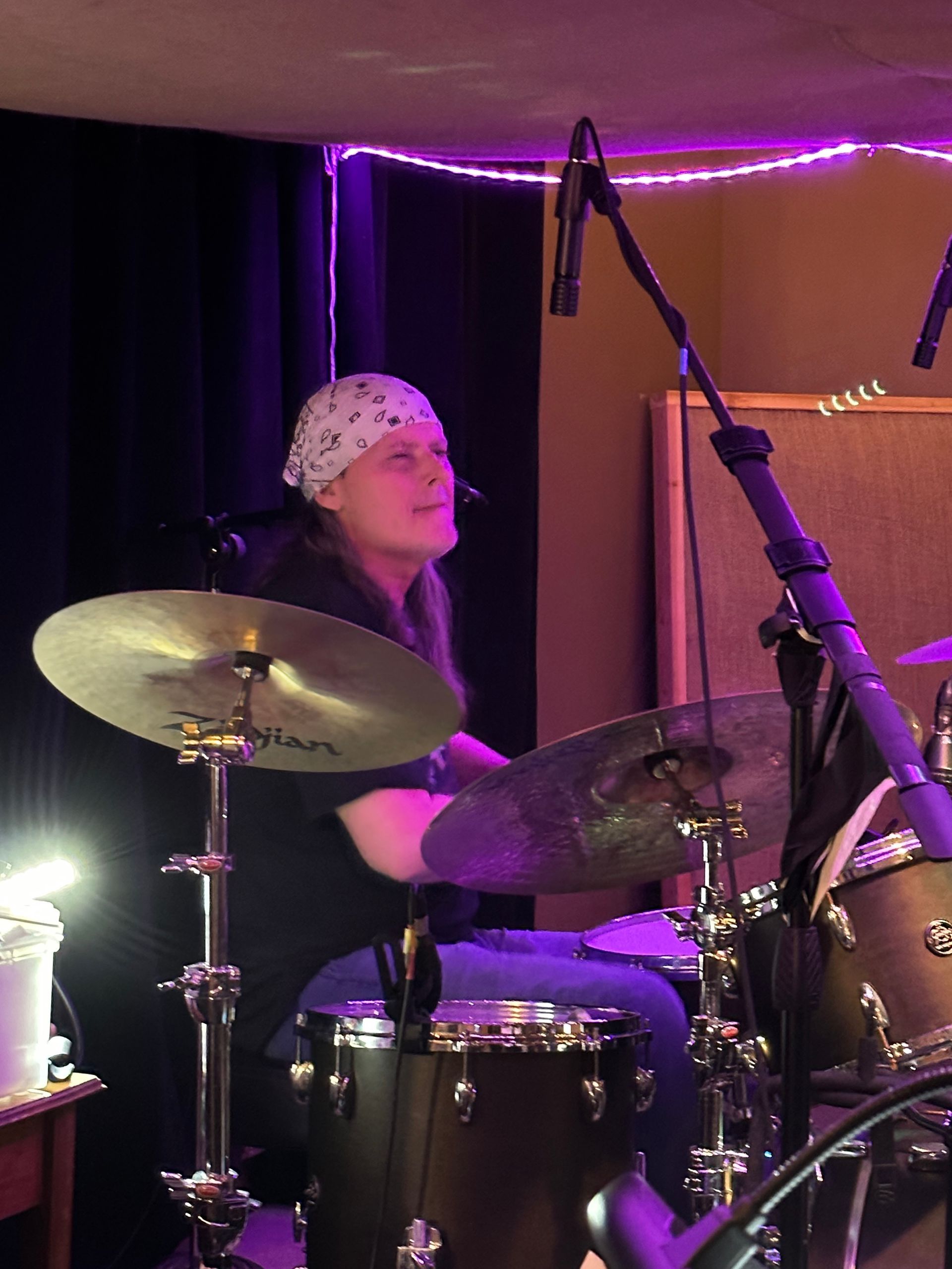A woman in a bandana is playing drums in a dark room