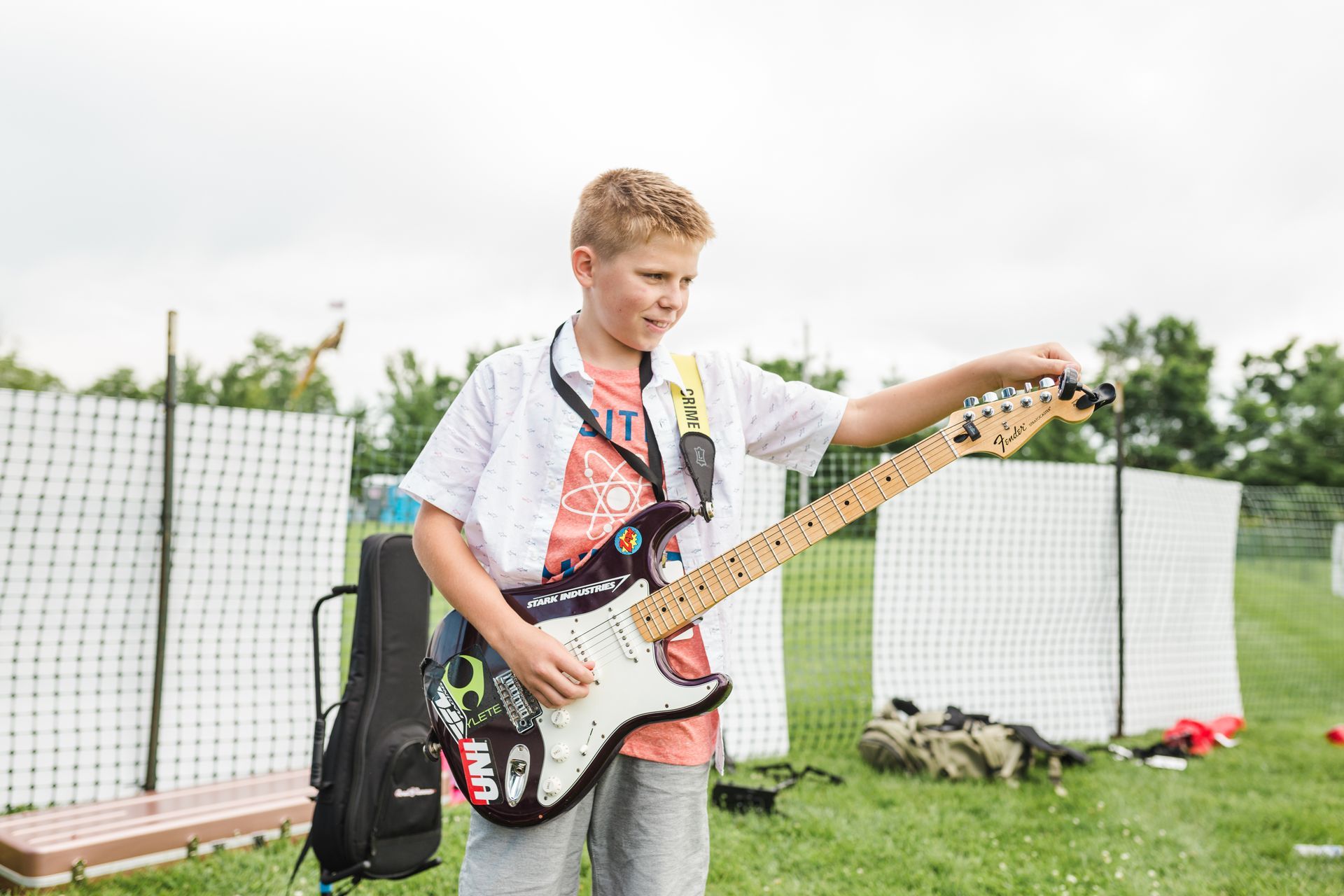 A young boy is playing an electric guitar in a field.