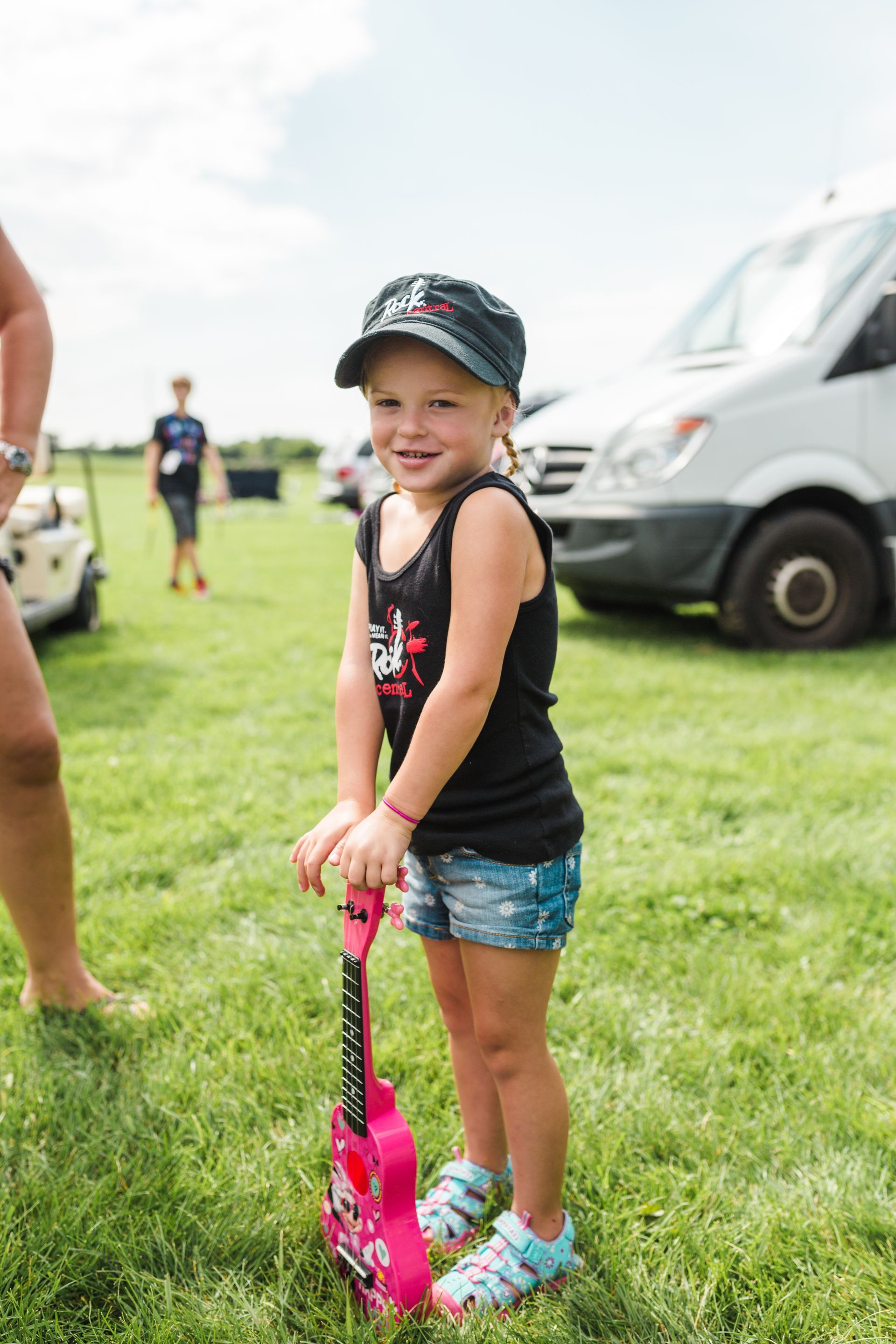A little girl is standing in the grass holding a pink guitar.