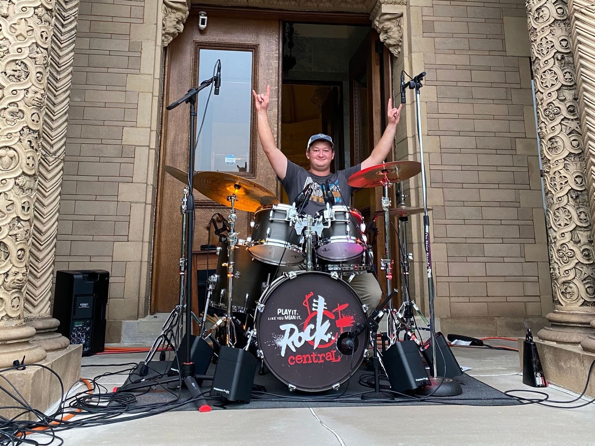 A man is standing in front of a drum set with his arms in the air.