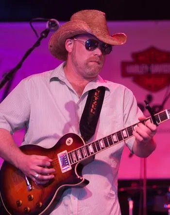 A man wearing a cowboy hat and sunglasses is playing a guitar