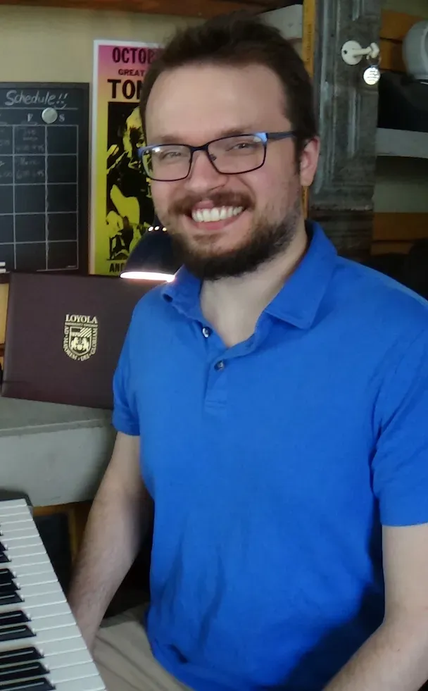A man wearing glasses and a blue shirt is sitting at a piano