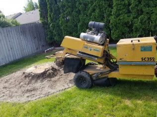 Yellow utility machine unloading a pile of sand in a grassy backyard beside a fence