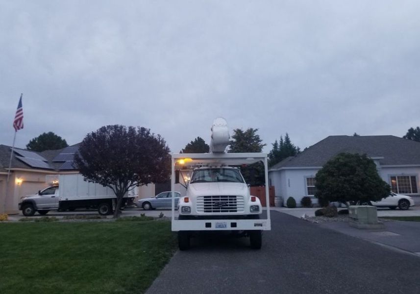 White broadcast truck parked on a suburban street at dusk, with a satellite dome and lit houses nearby