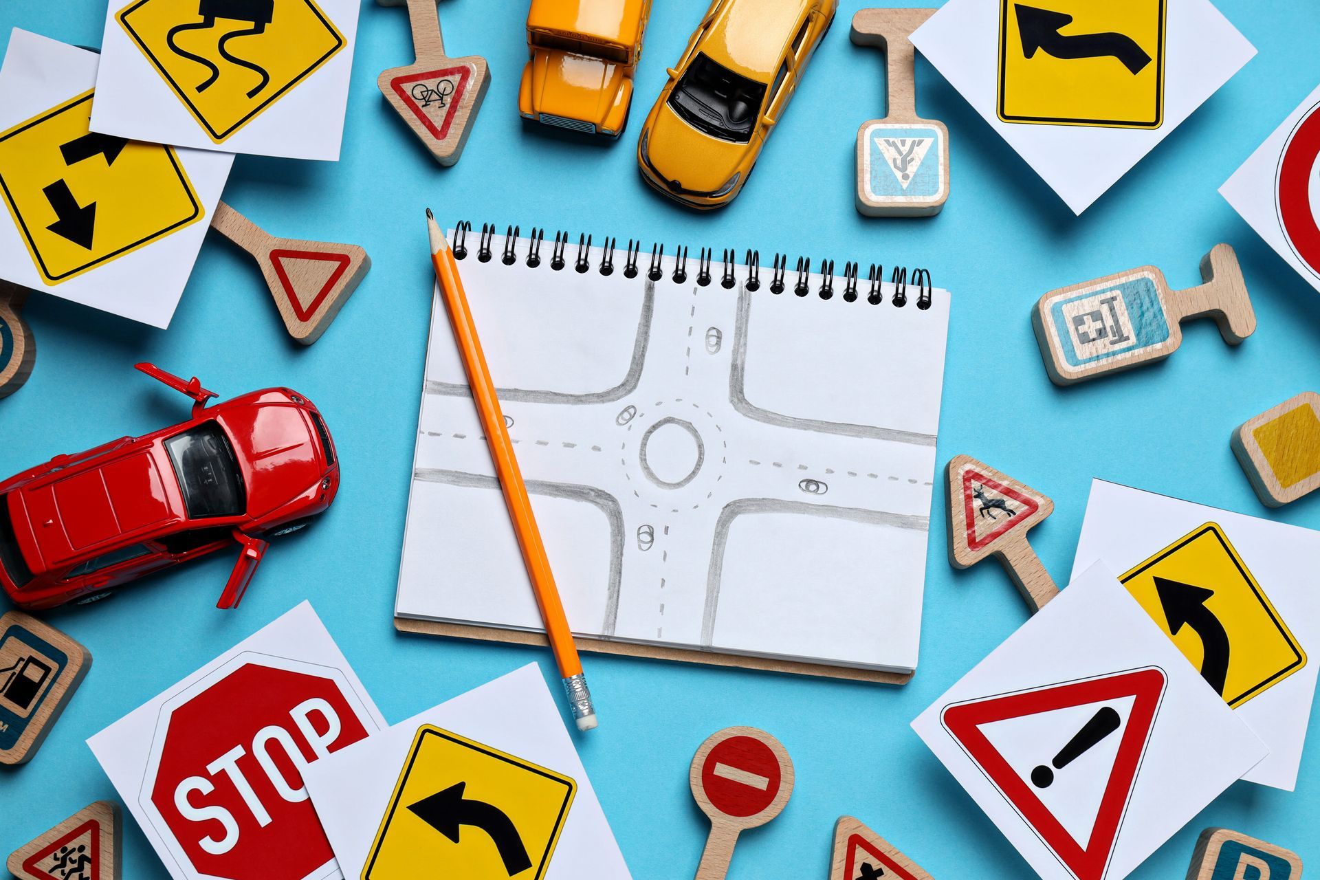 Toy cars and road signs surrounding a sketchpad with a drawn intersection on a blue background
