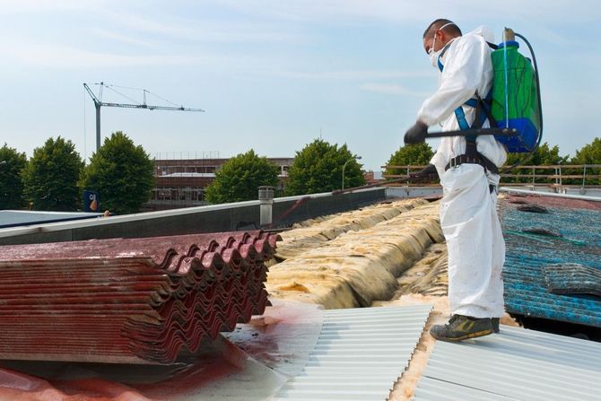 Worker in protective suit spraying chemicals on a rooftop covered with stacked materials