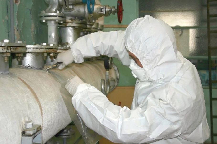 Worker in white protective suit inspecting industrial pipes and equipment in a factory.