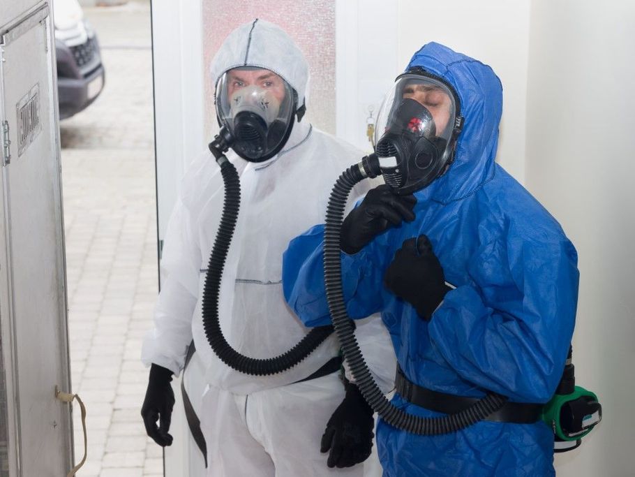 Two people in protective suits and respirators standing in a hallway.