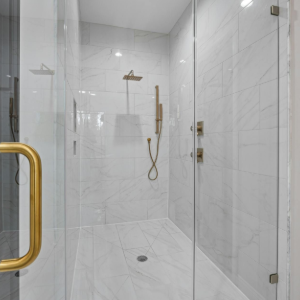 Modern walk-in shower with white tile walls, glass door, and gold handles