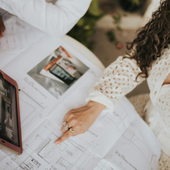 Two people reviewing floor plans at a table with a tablet and coffee