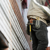 Worker with tool belt standing beside a slanted corrugated metal wall on a construction site