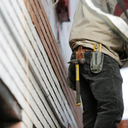 Worker with tool belt standing beside a slanted corrugated metal wall on a construction site