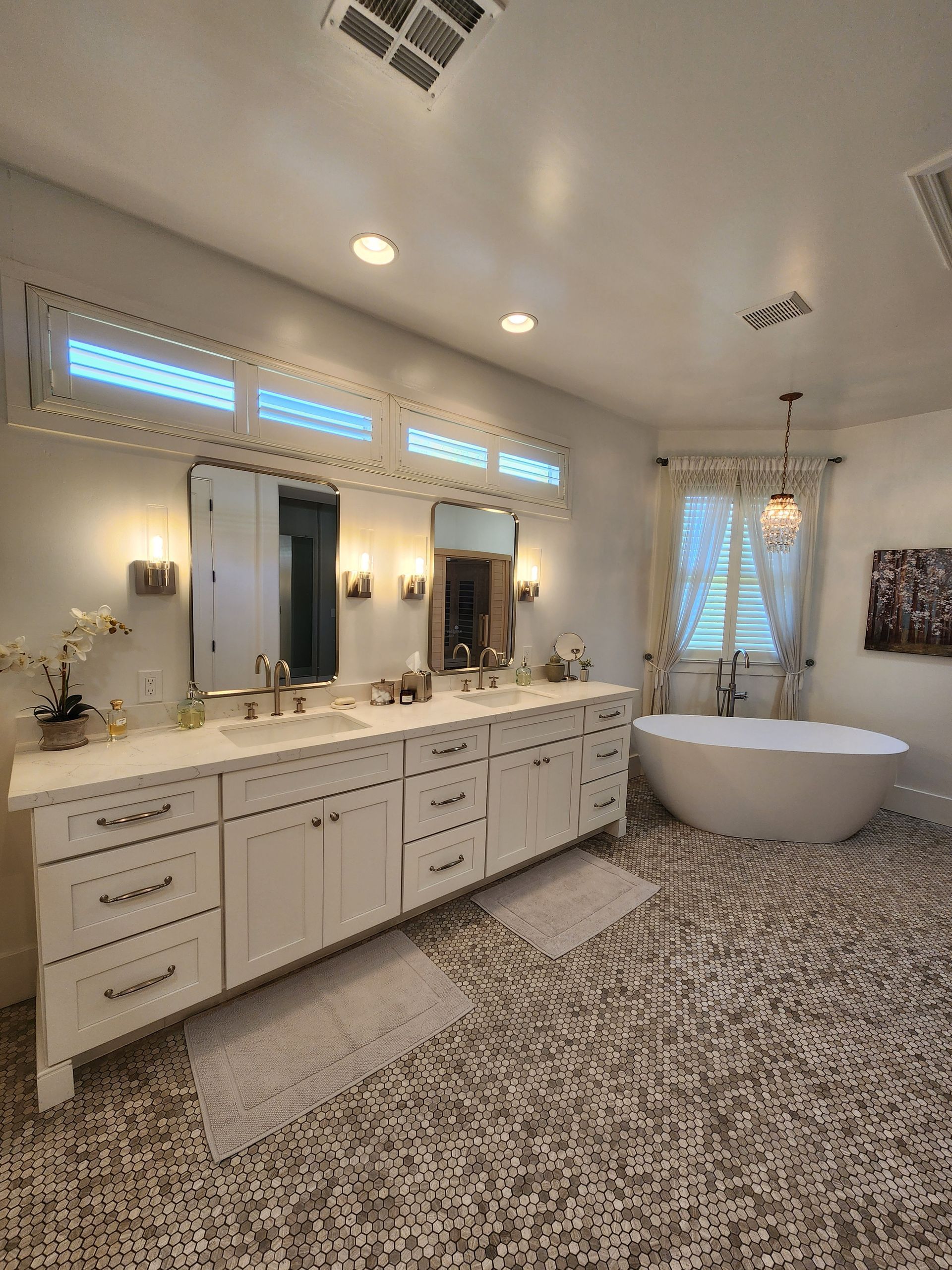 Elegant white bathroom with double vanity, round bathtub, mirrors, and patterned tile floor