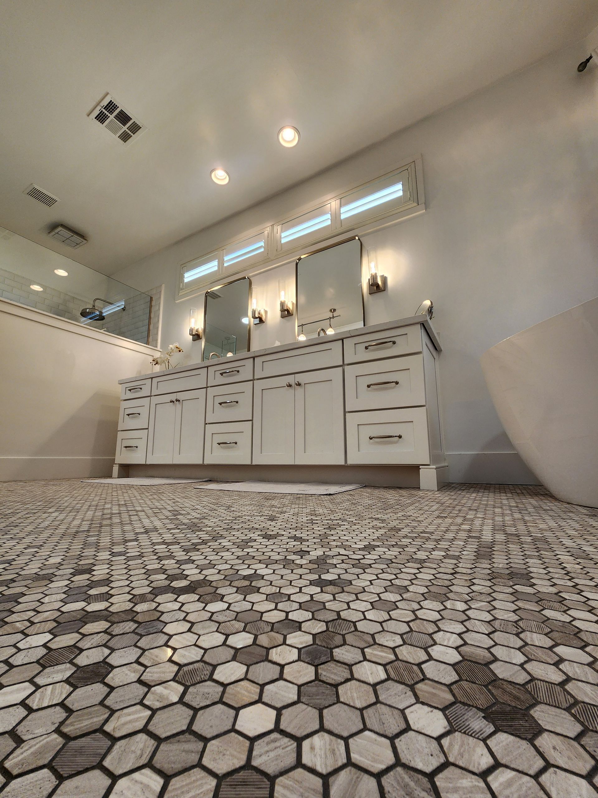 Spacious white bathroom with double vanity, mirrors, and hexagon tile floor.