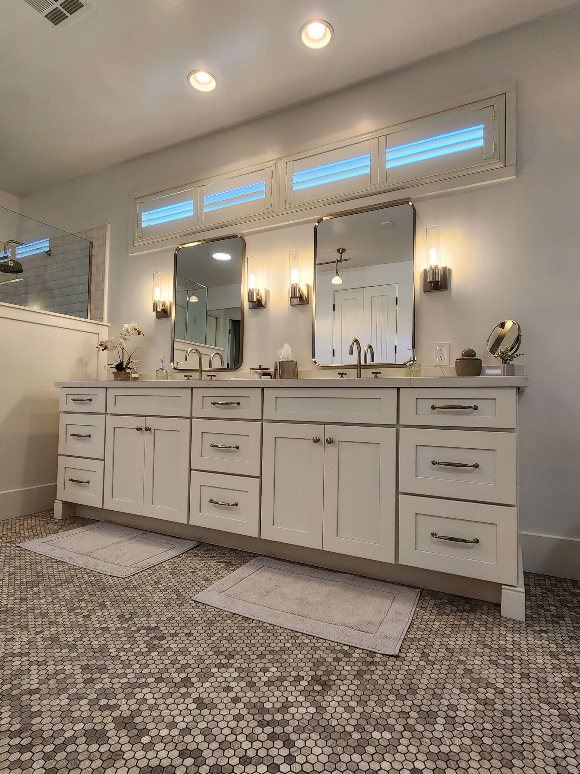 Bright, elegant bathroom vanity with two mirrors, white cabinets, wall sconces, and patterned rug