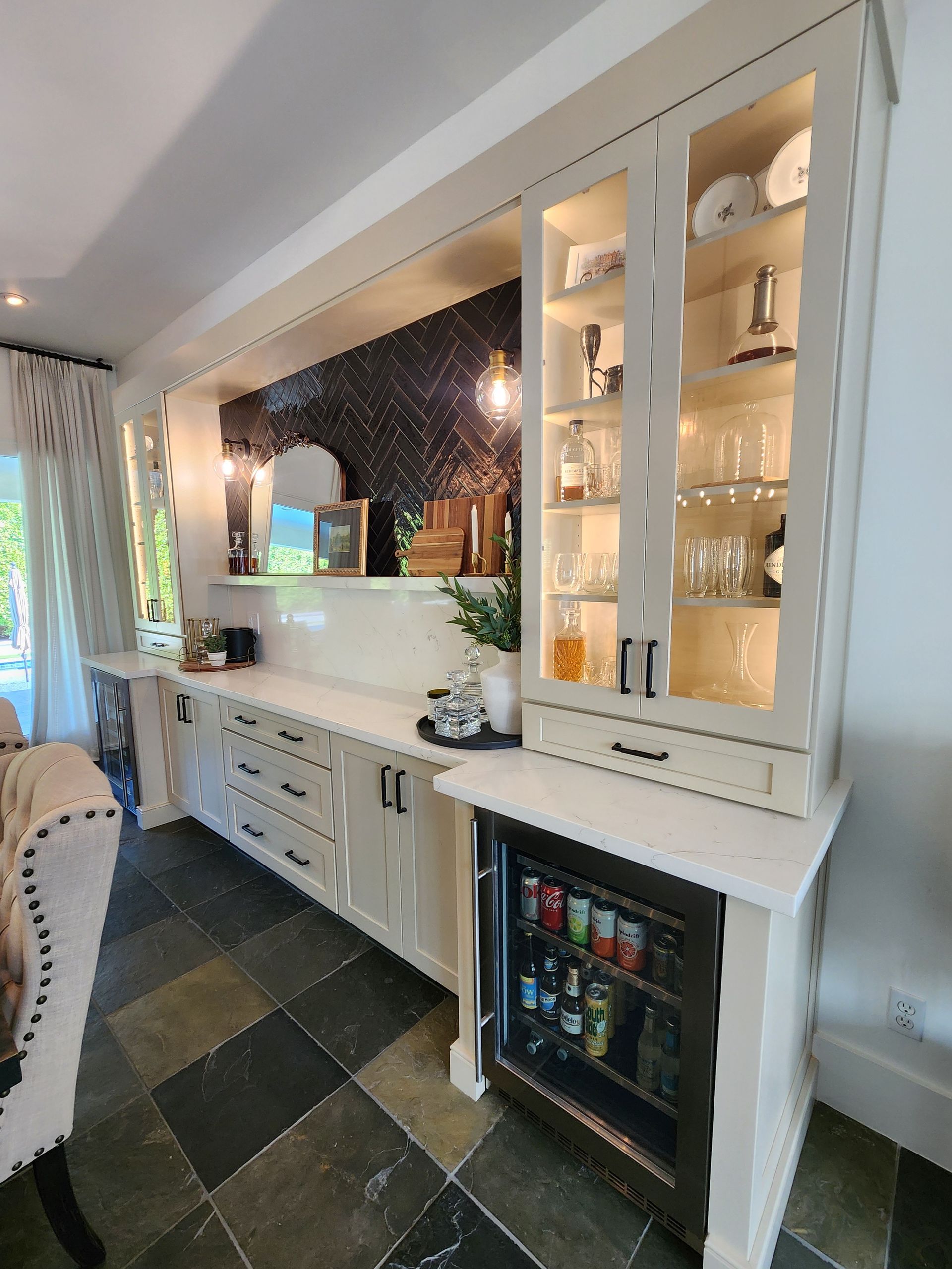 White kitchen buffet with glass cabinets, granite backsplash, and a small built-in beverage fridge under the counter