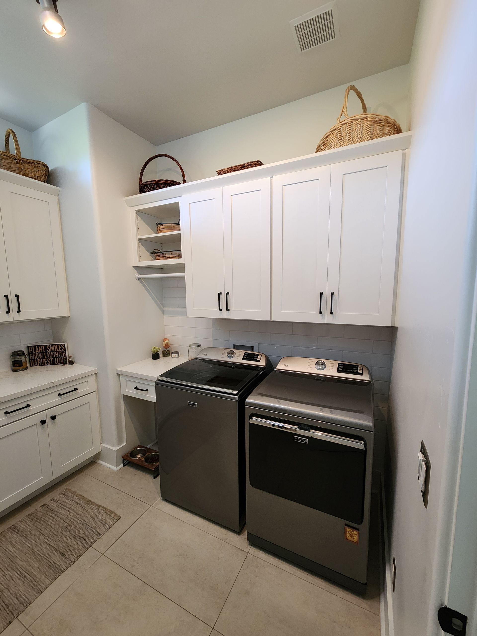 Laundry room with white cabinets, black washer and dryer, and woven baskets on top shelves.