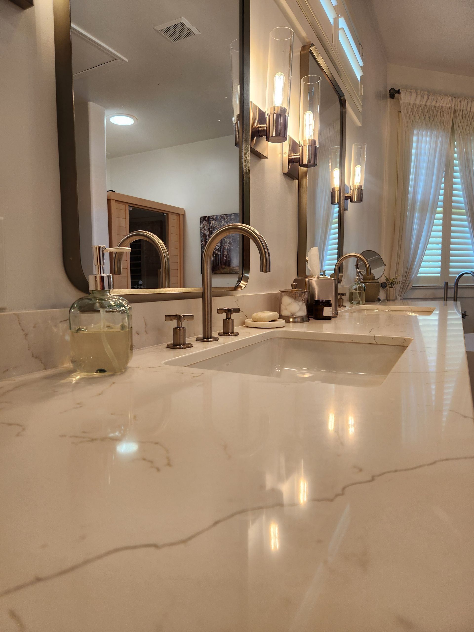 Elegant bathroom vanity with marble countertop, chrome faucet, wall sconces, and a window with blinds