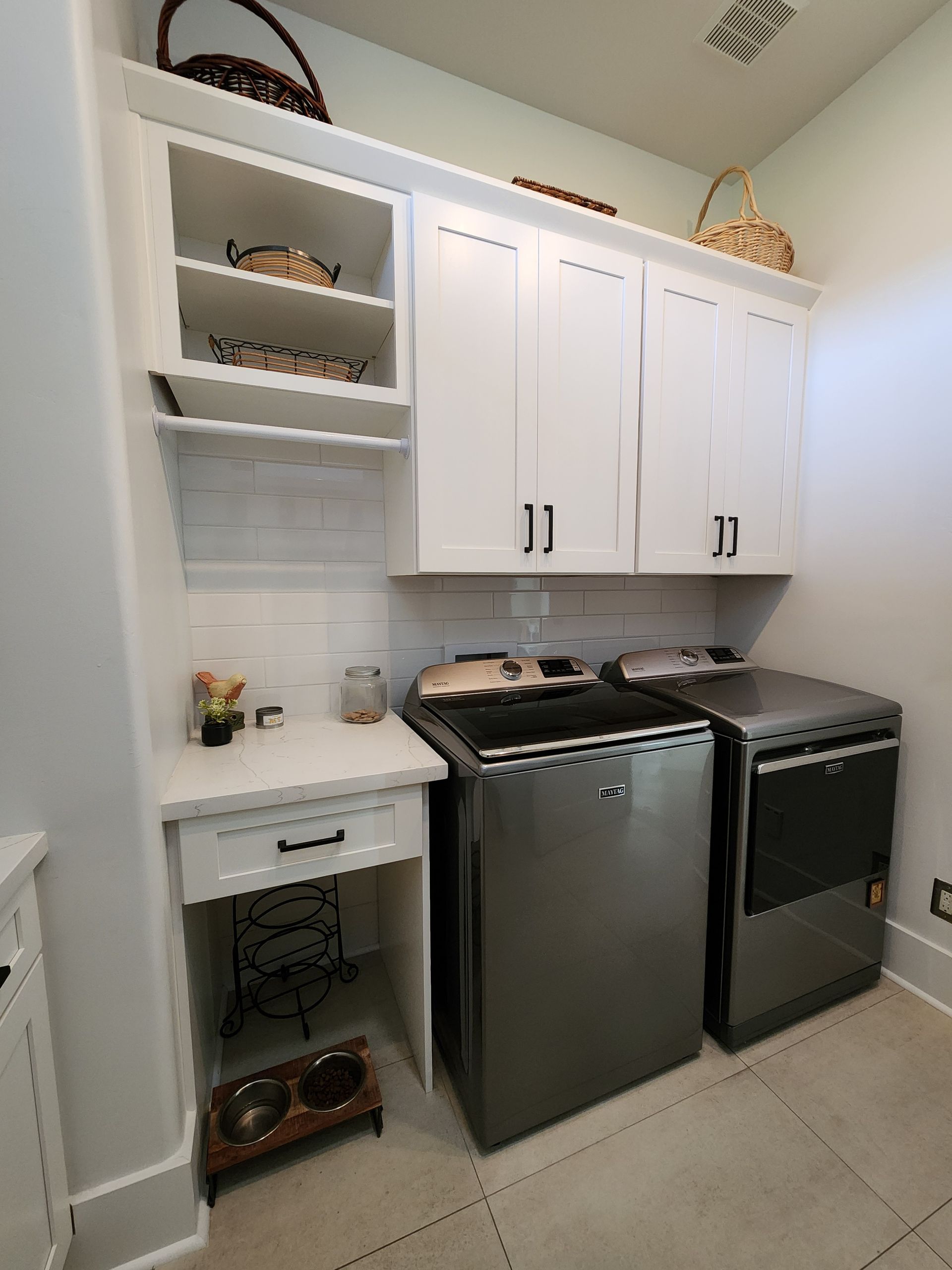 Small white kitchen with stove, dishwasher, sink, cabinets, open shelves, and tiled floor.