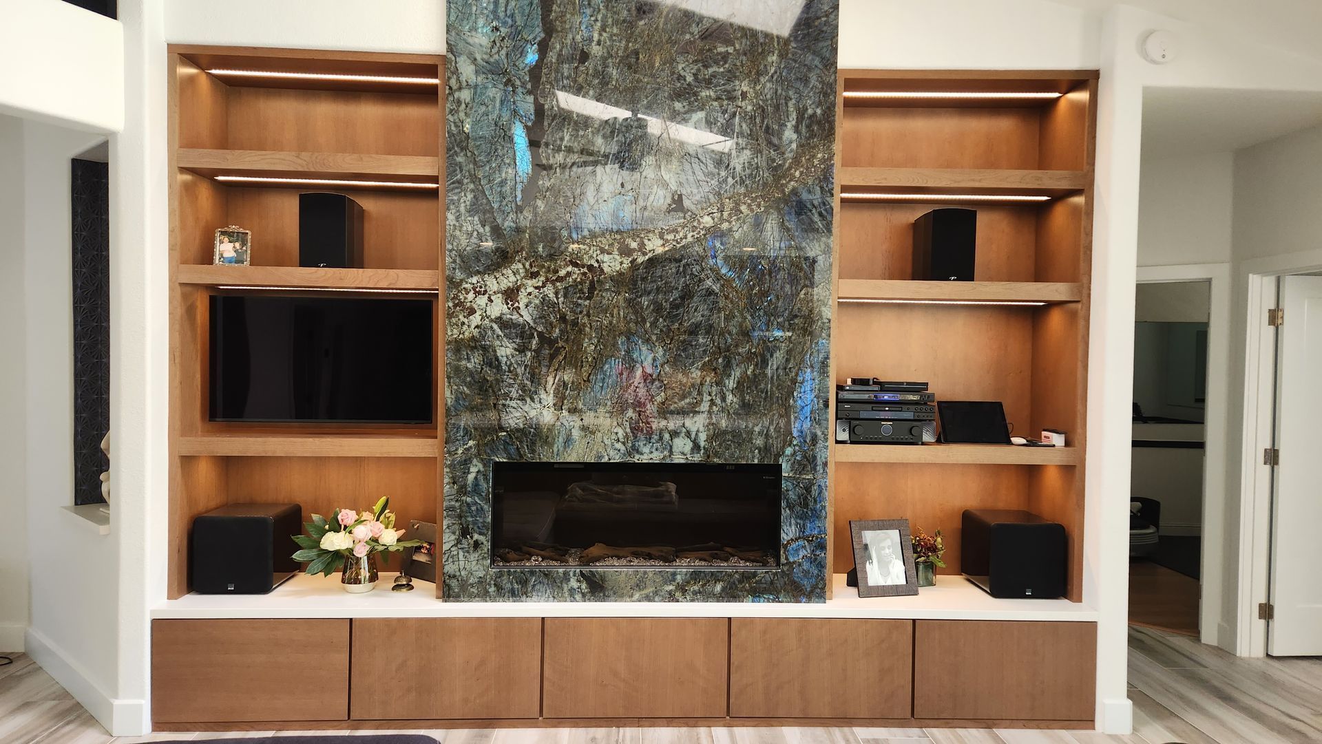 Modern living room wall with built-in wooden shelves and a large marble fireplace center.
