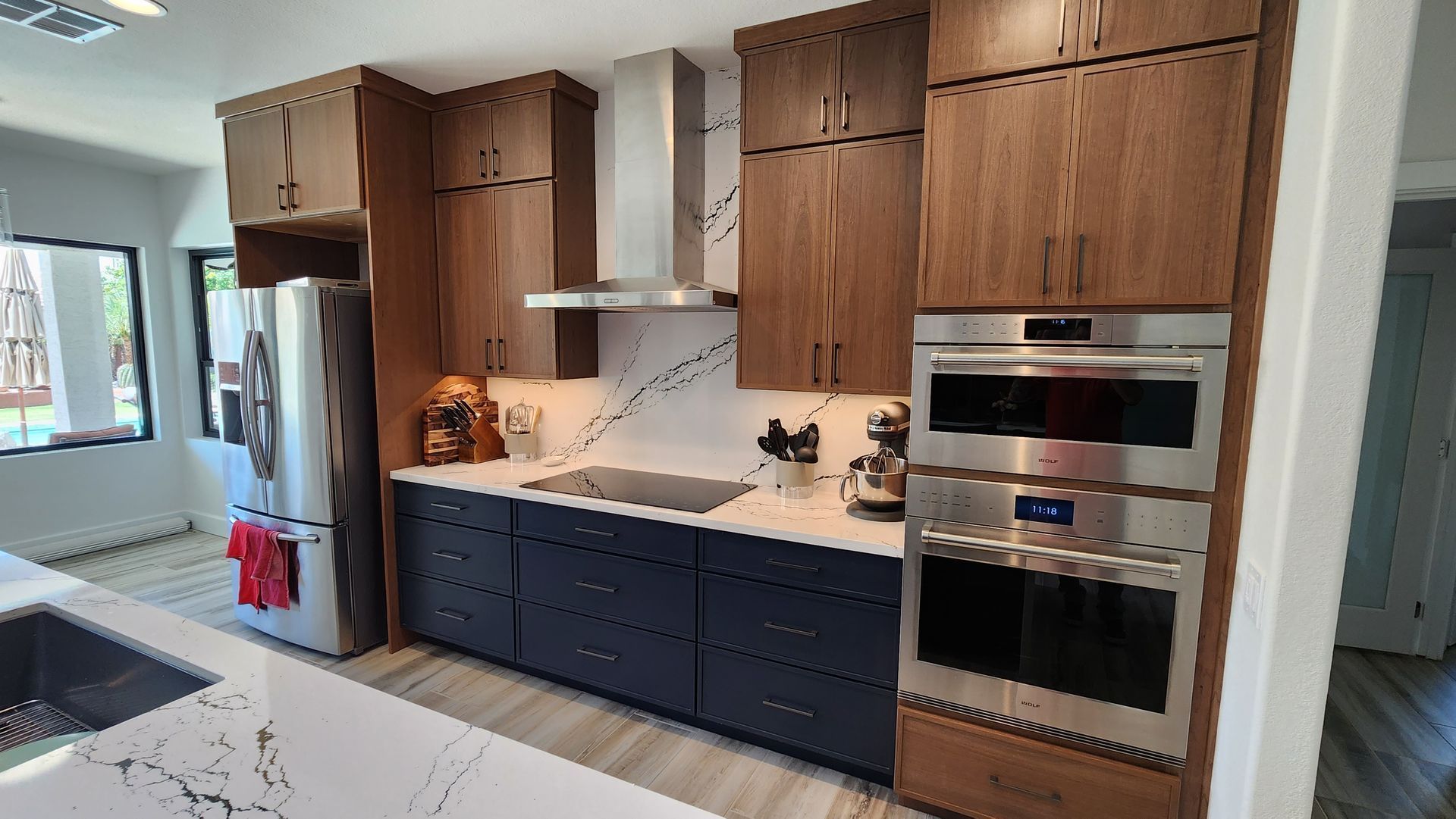 Modern kitchen with wood cabinets, dark blue lower drawers, white counters, stainless appliances, and a refrigerator.