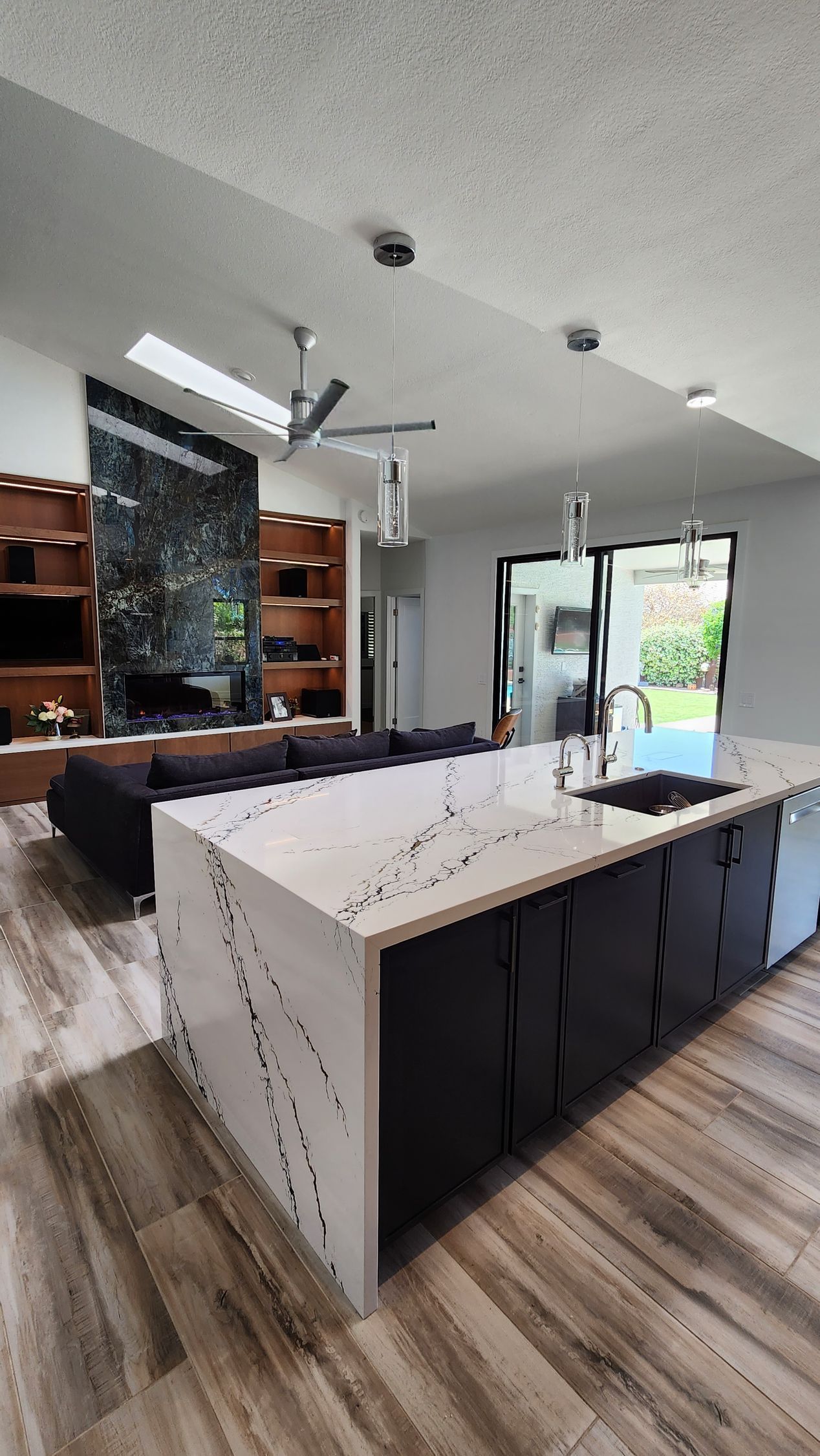 Modern kitchen with white island, dark cabinets, wood floors, and large glass doors to a patio.