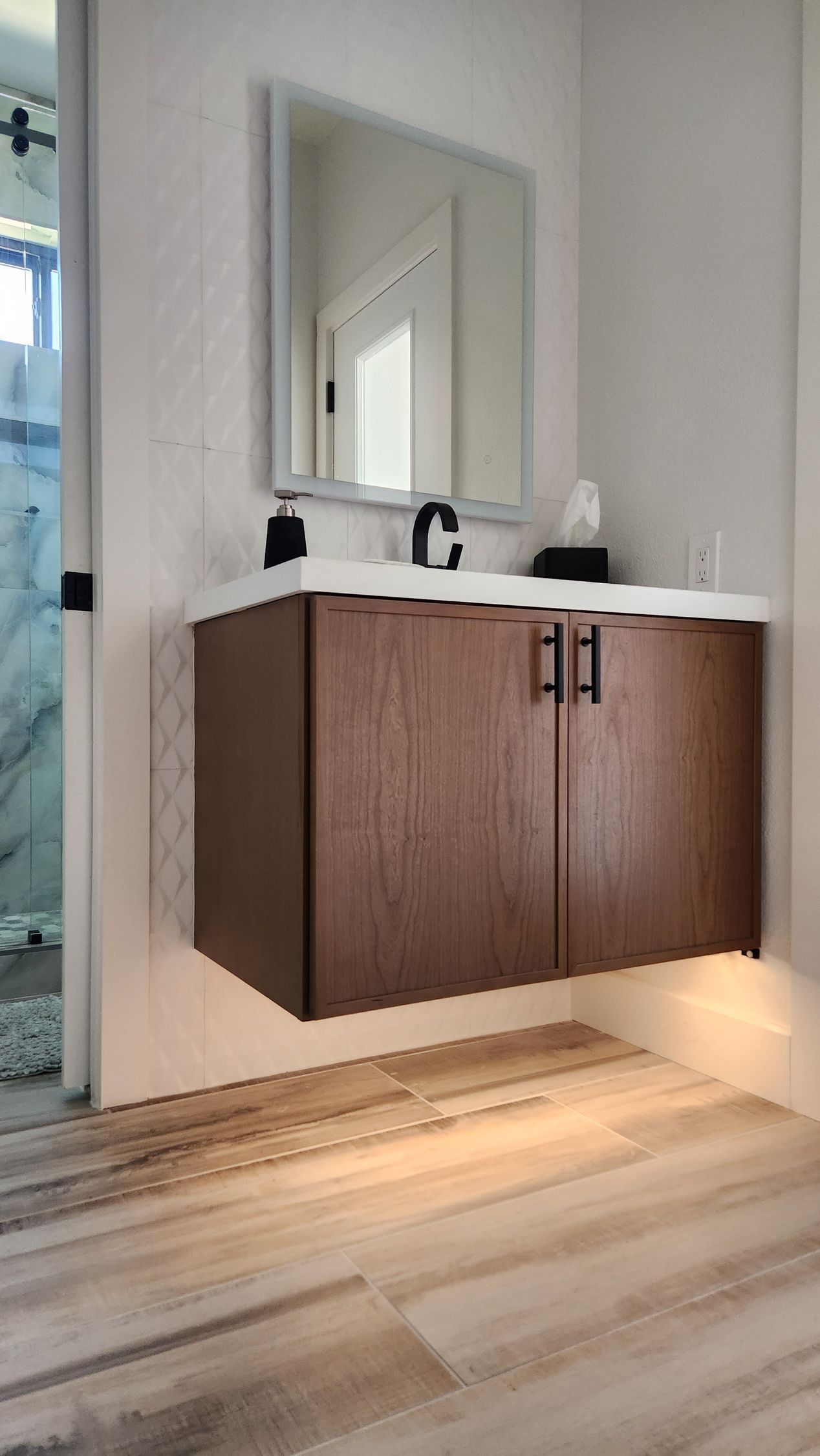 Modern bathroom vanity with dark wood cabinets, white countertop, mirror, and warm under-cabinet lighting.