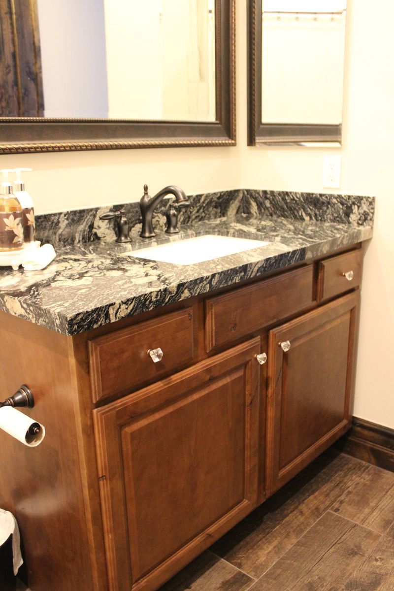Bathroom vanity with dark wood cabinets, black granite countertop, sink, and wall mirror