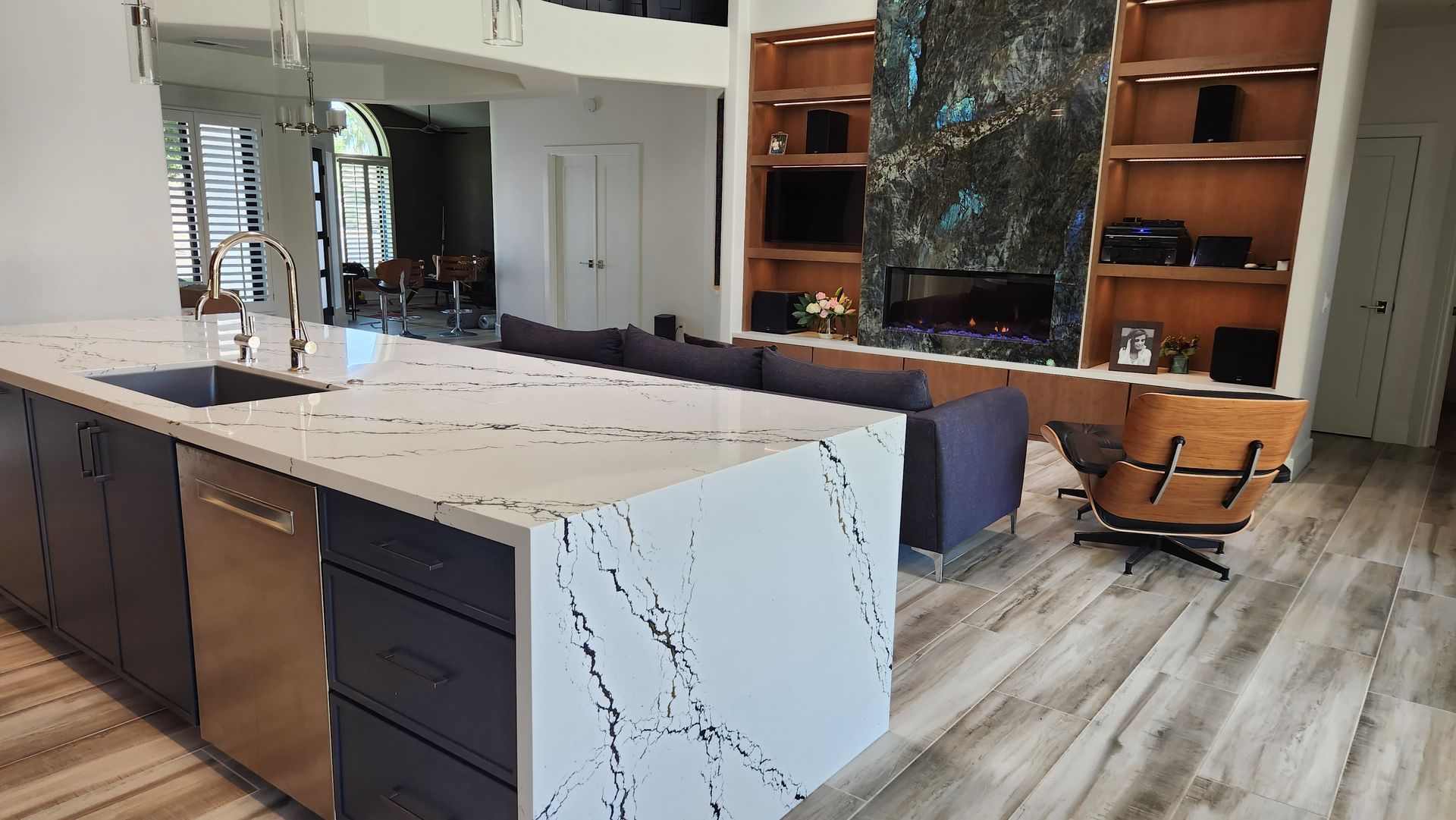 Modern kitchen with white marble island, dark cabinets, and a built-in window seat in the background