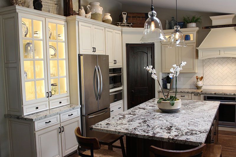 Elegant cream kitchen with stainless appliances, glass-front cabinets, and a marble island with flowers.