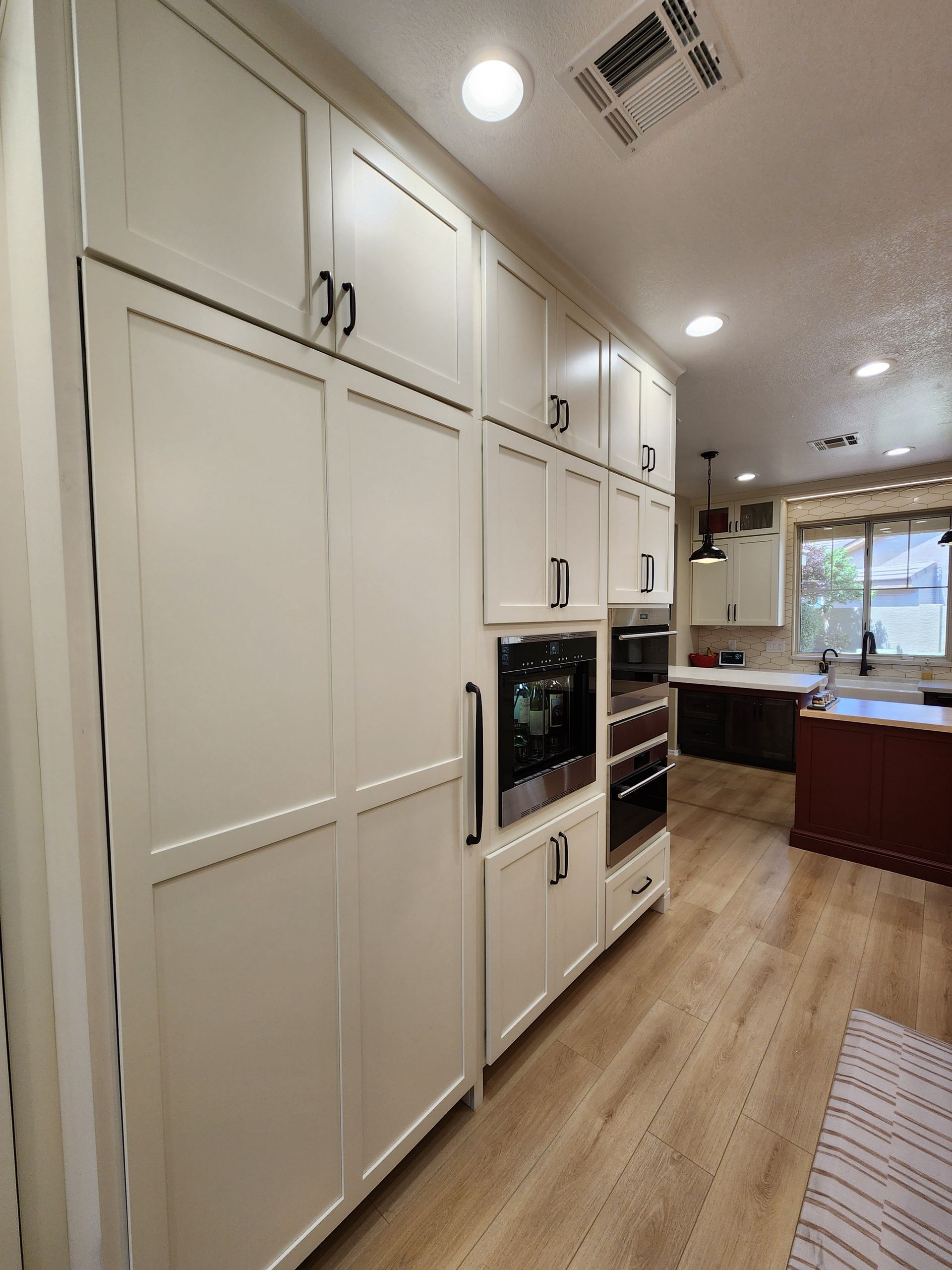 Bright kitchen with white cabinets, built-in oven, wood floors, and a window view.