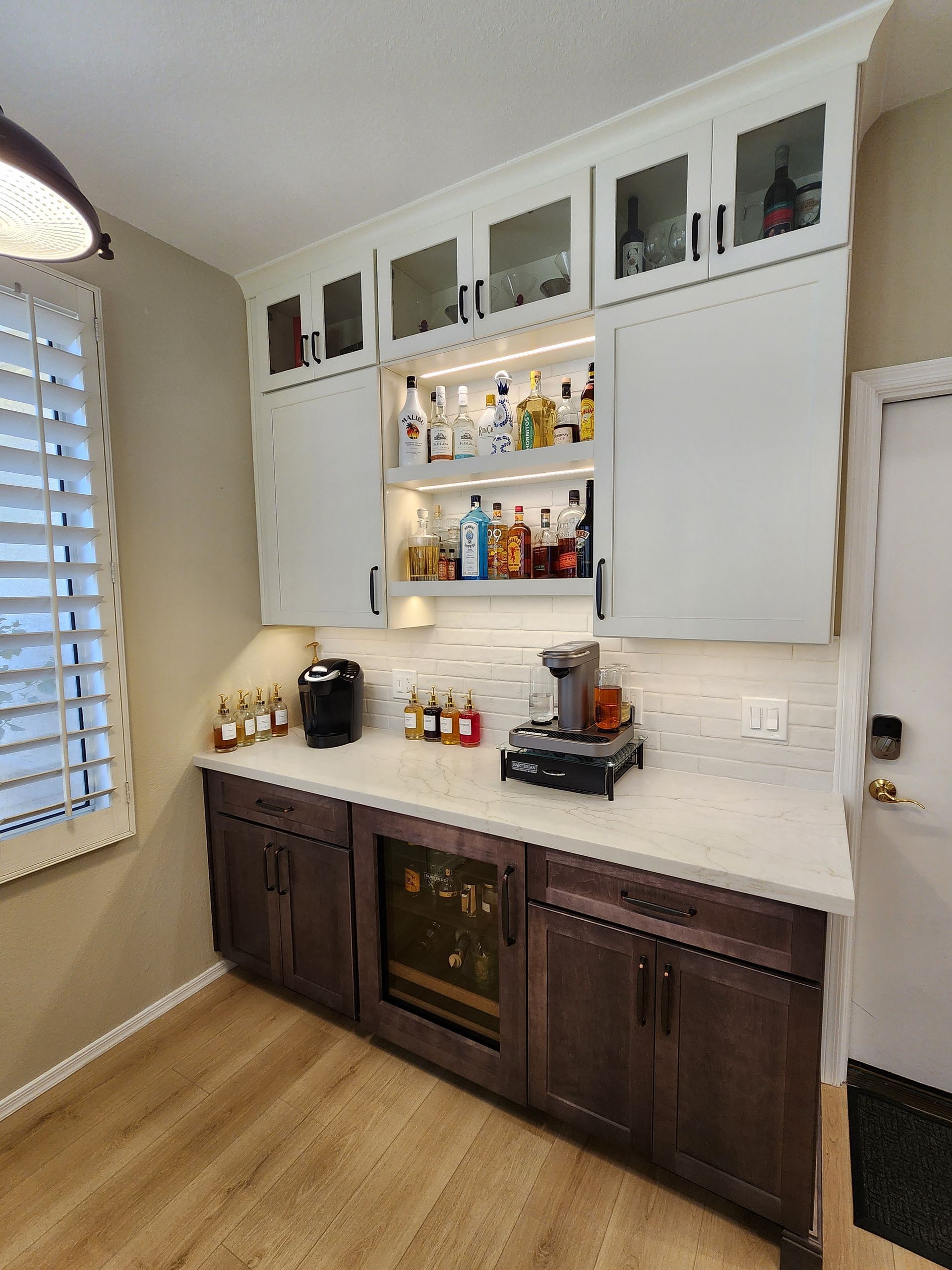 Built-in kitchen bar with white cabinets, dark wood base cabinets, countertop, and shelves with bottles.