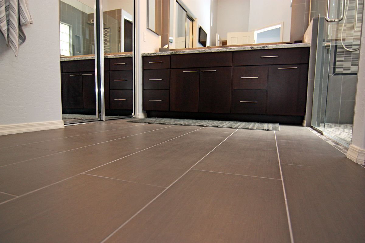 Low-angle view of a bathroom with dark vanity cabinets, mirror, and large brown floor tiles.
