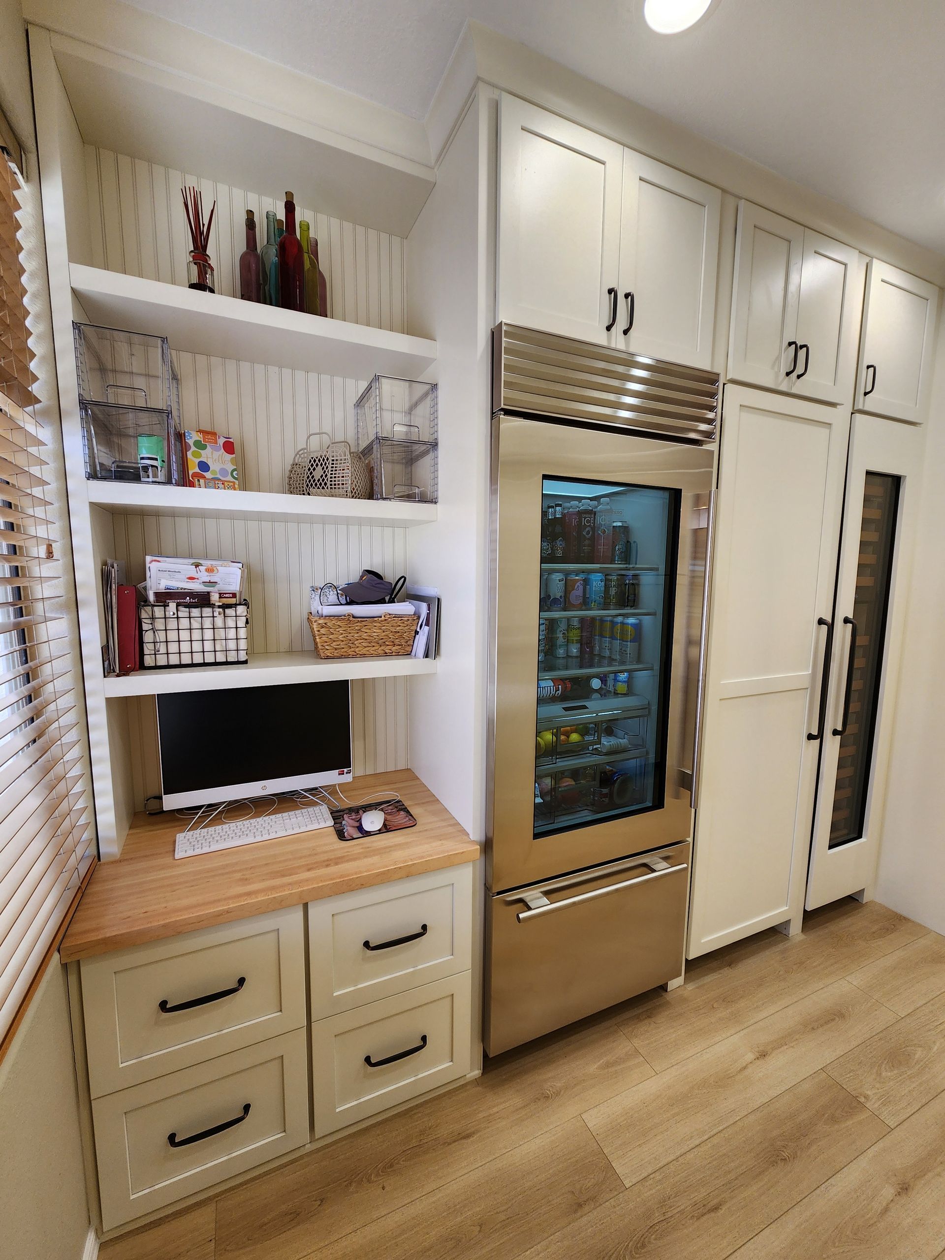 Built-in white pantry with shelves, drawers, and a stainless steel fridge in a bright kitchen.