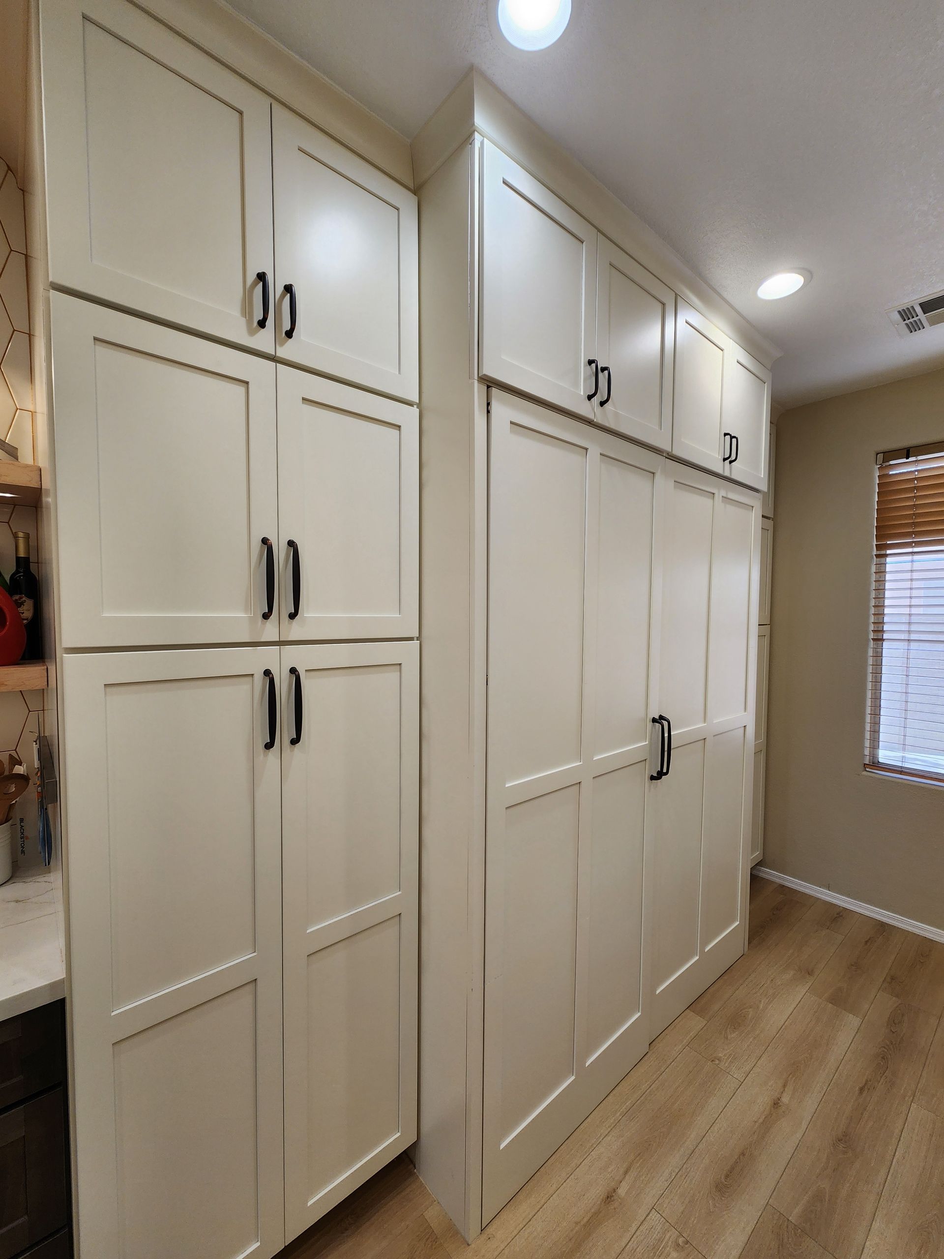 Built-in white bedroom closets with black handles along a hallway wall, lit by ceiling lights.