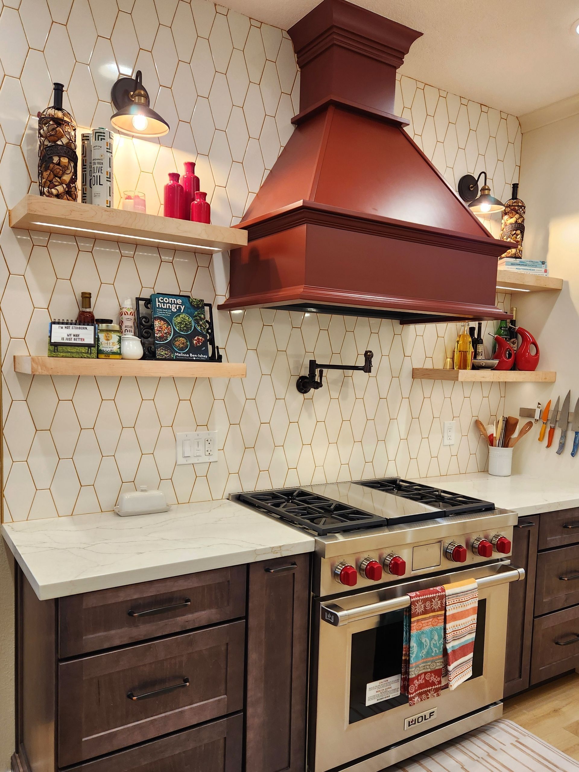 Modern kitchen with cream cabinets, burgundy range hood, open shelves, and stainless steel stove.