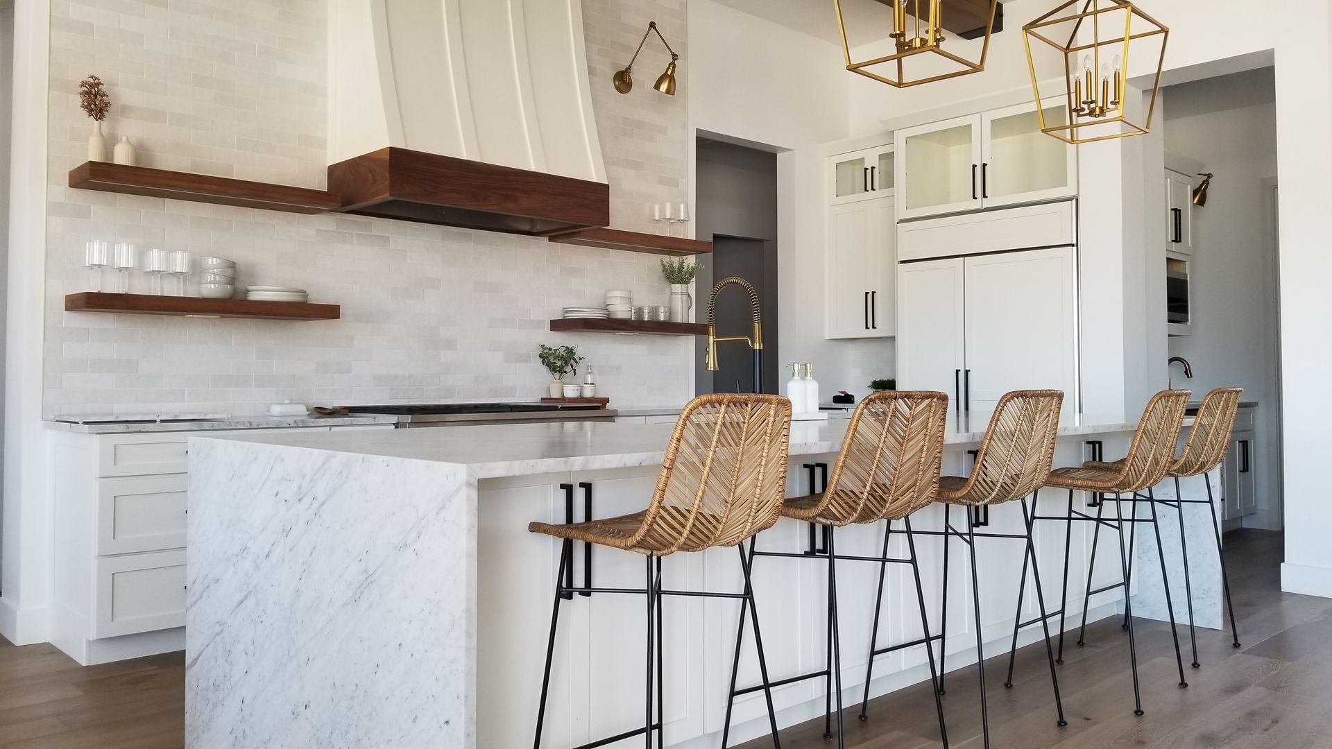 Bright modern kitchen with white cabinets, marble island, and woven barstools under pendant lights