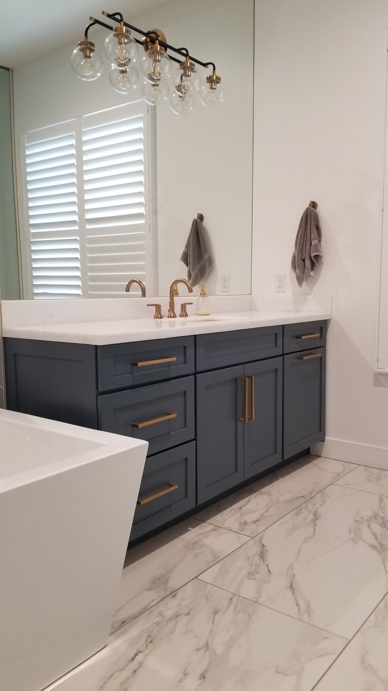 Blue vanity bathroom with gold fixtures, white sink, window shutters, and marble floor