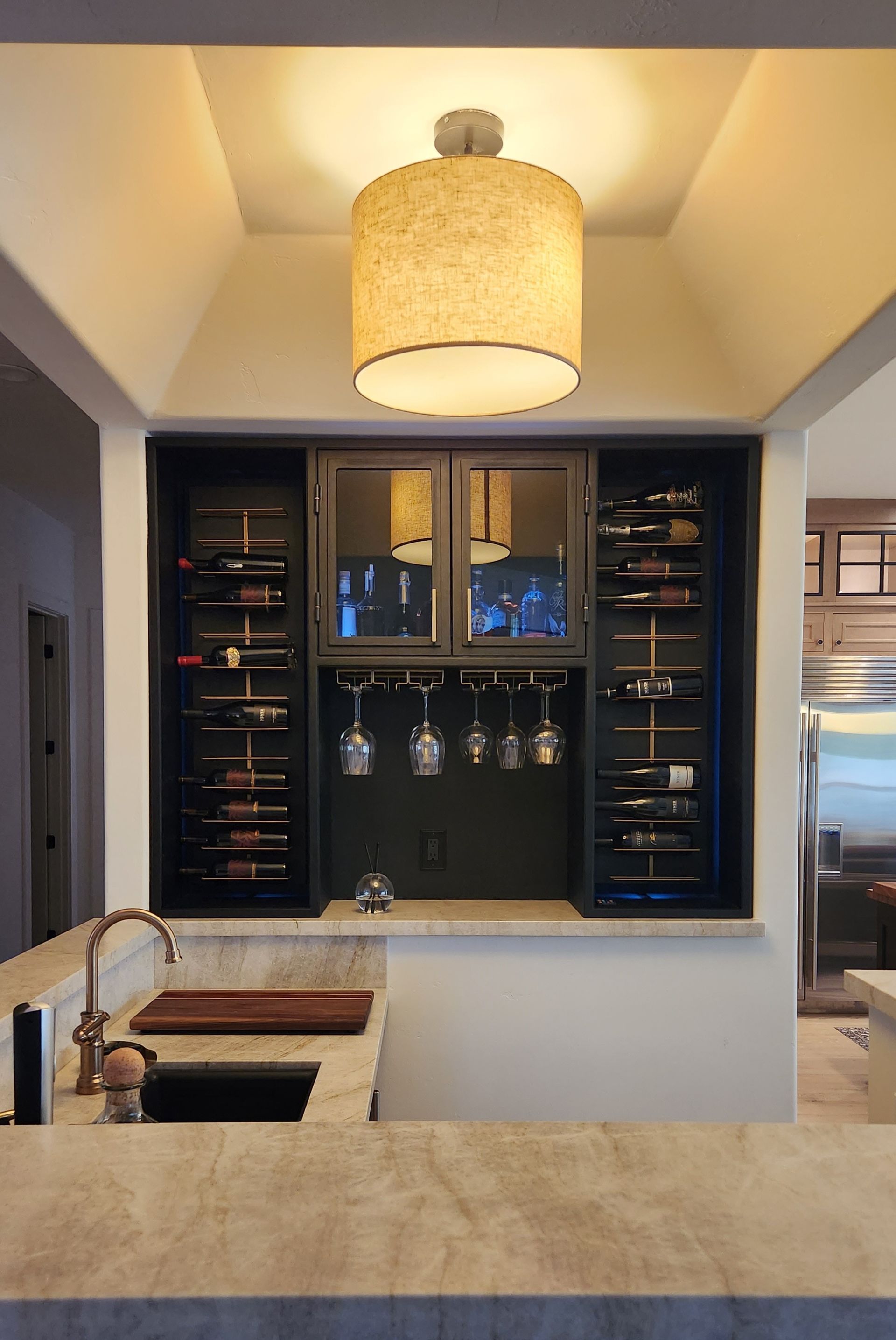 Modern kitchen with a pass-through bar, wine racks, hanging glasses, and a woven pendant light