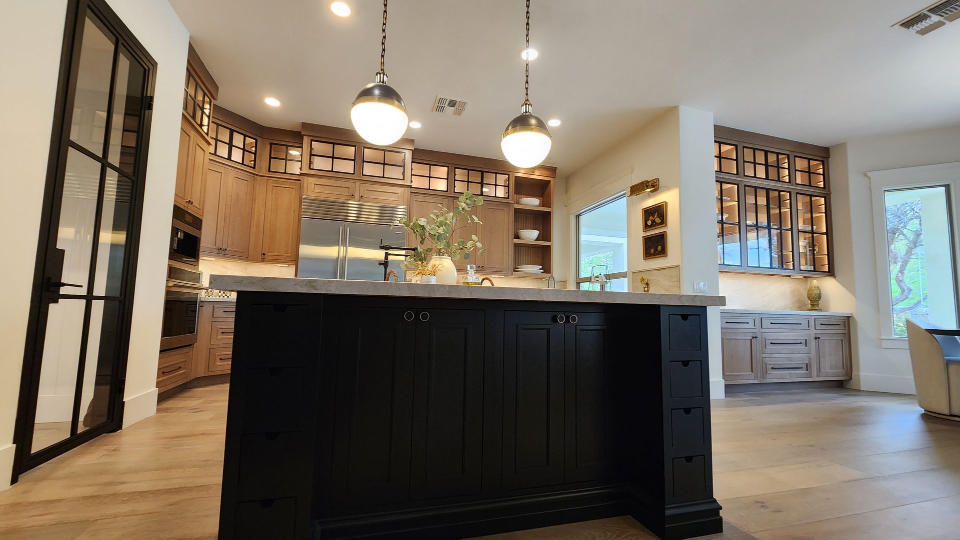 Modern kitchen with black island, pendant lights, wood cabinets, and light hardwood floors