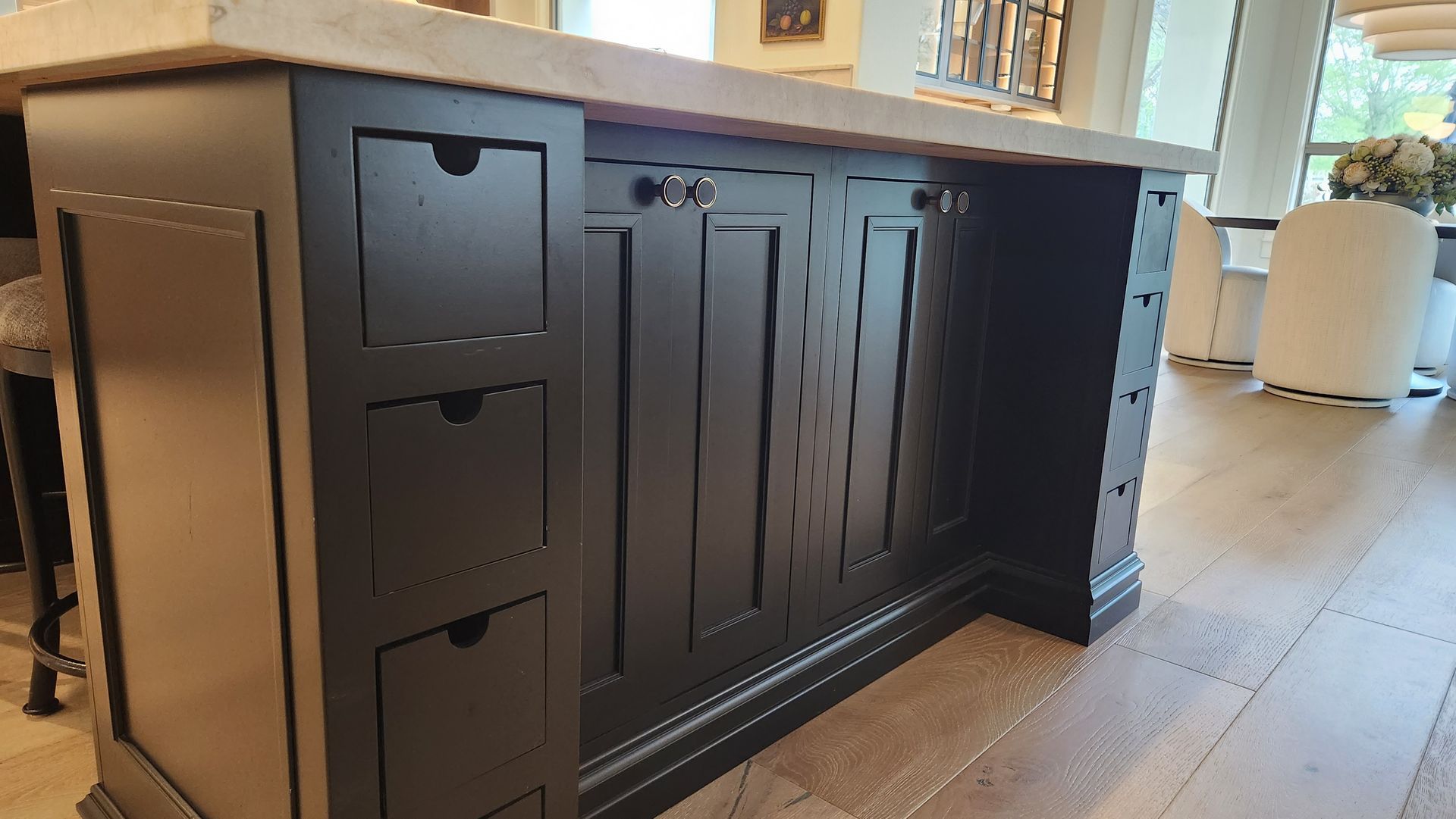 Black kitchen island cabinet with drawers and paneled doors on a light wood floor under a countertop