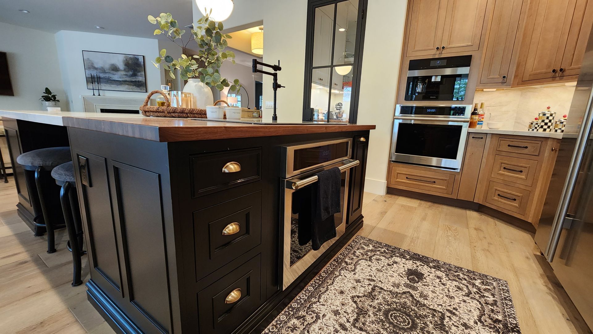 Modern kitchen with dark island, wood cabinets, built-in oven, and patterned rug