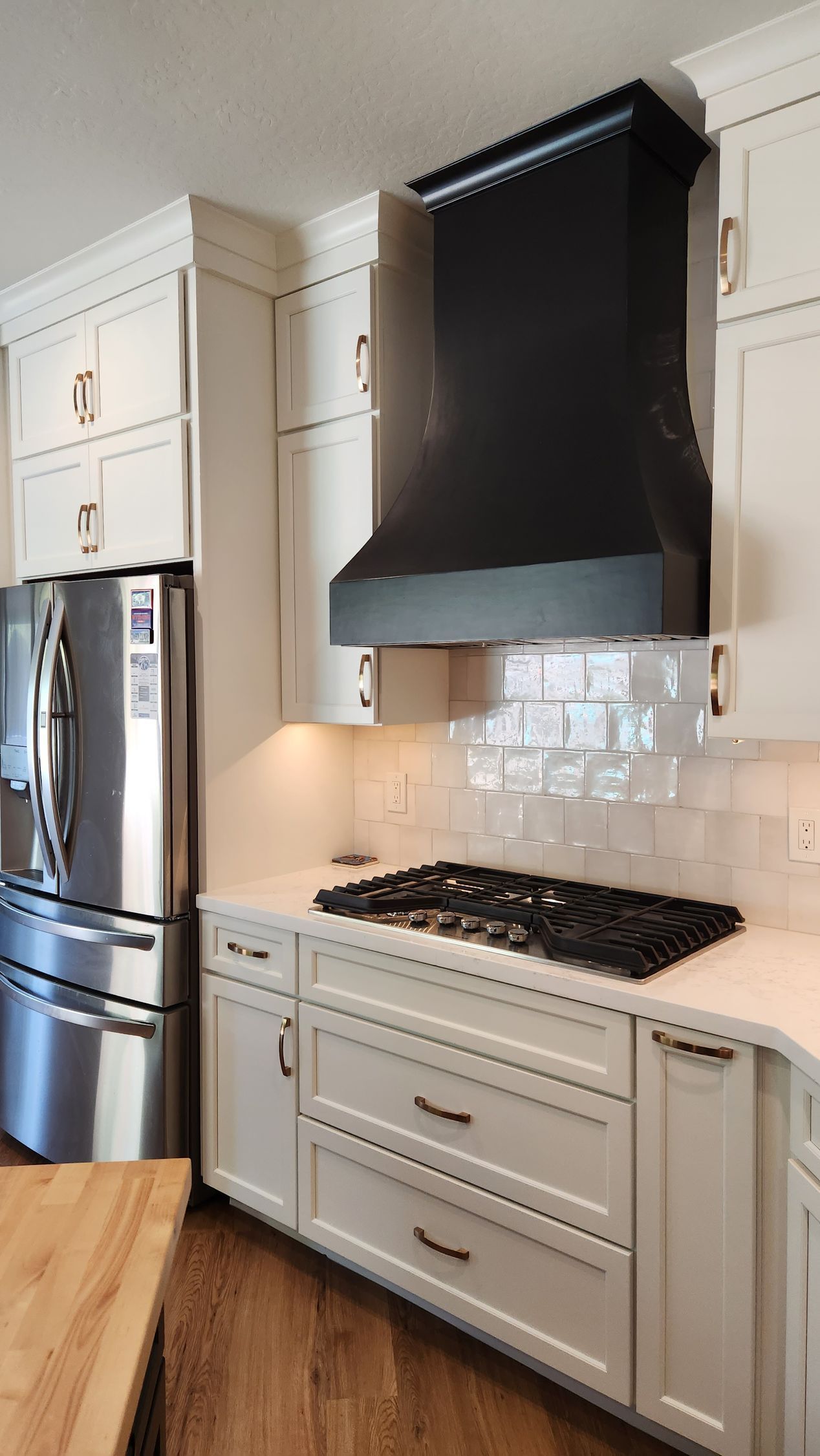 Modern white kitchen with stainless fridge, black range hood, gas stove, and marble-style backsplash.