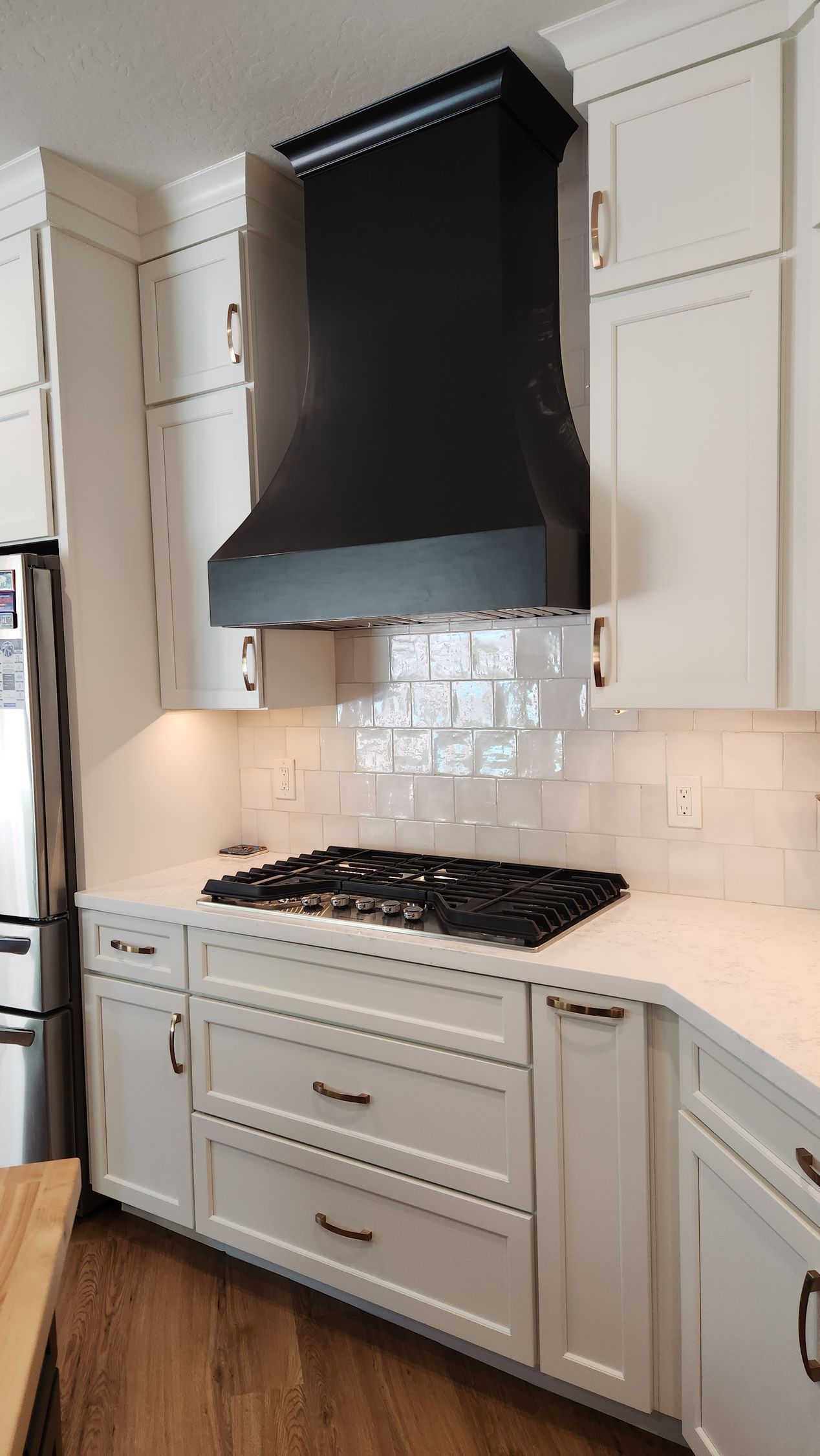 White kitchen with a black range hood, gas stove, and marble-look backsplash.