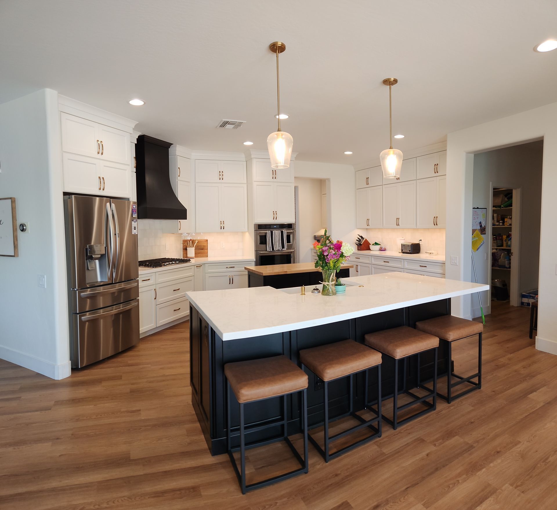Modern kitchen with white cabinets, stainless steel appliances, a large island, and four bar stools on wood flooring