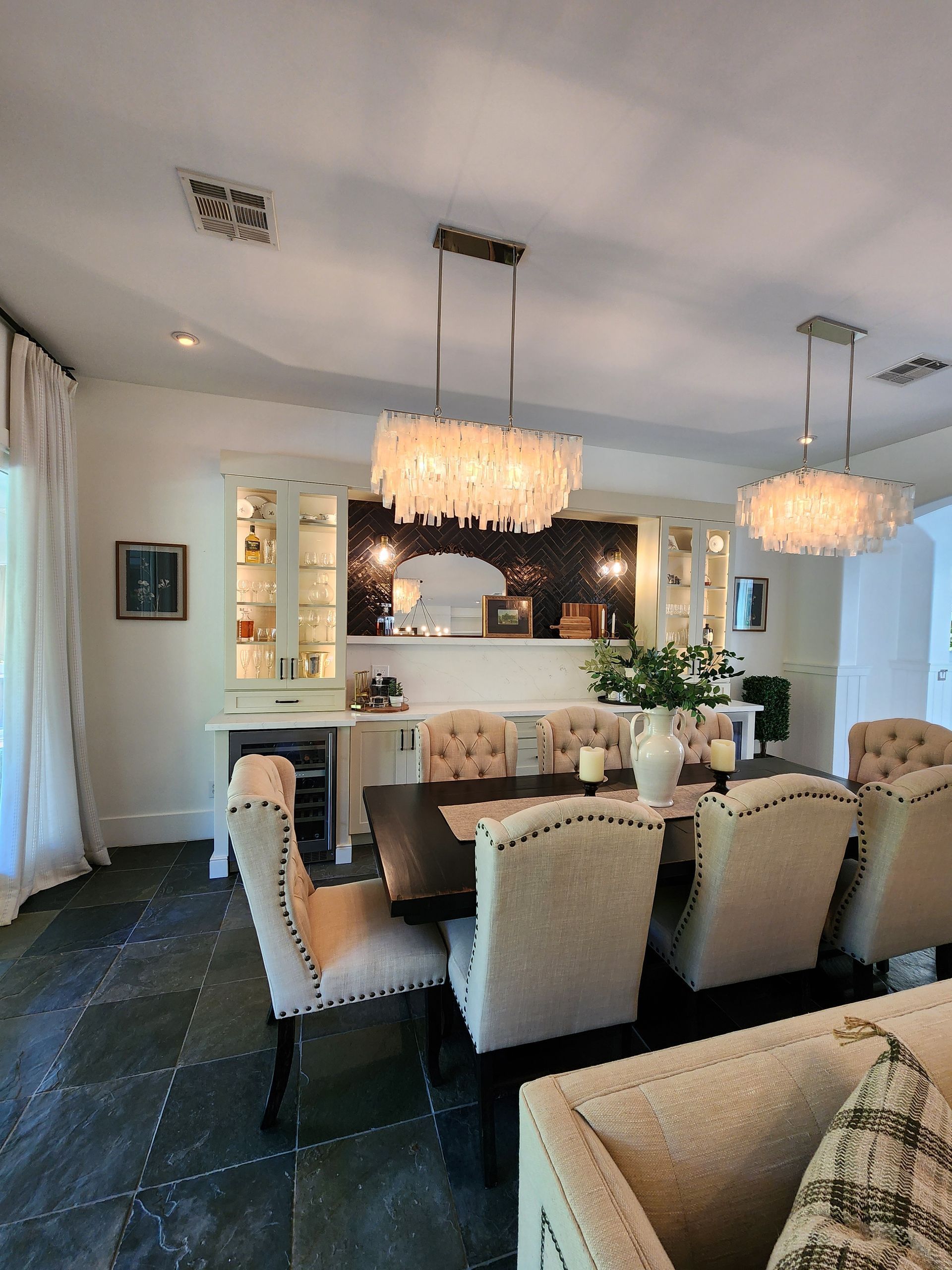 Elegant dining room with chandelier lighting, mirrored wall, and upholstered chairs around a long table.