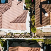 Aerial view of a suburban street lined with terracotta-roofed houses and parked cars.